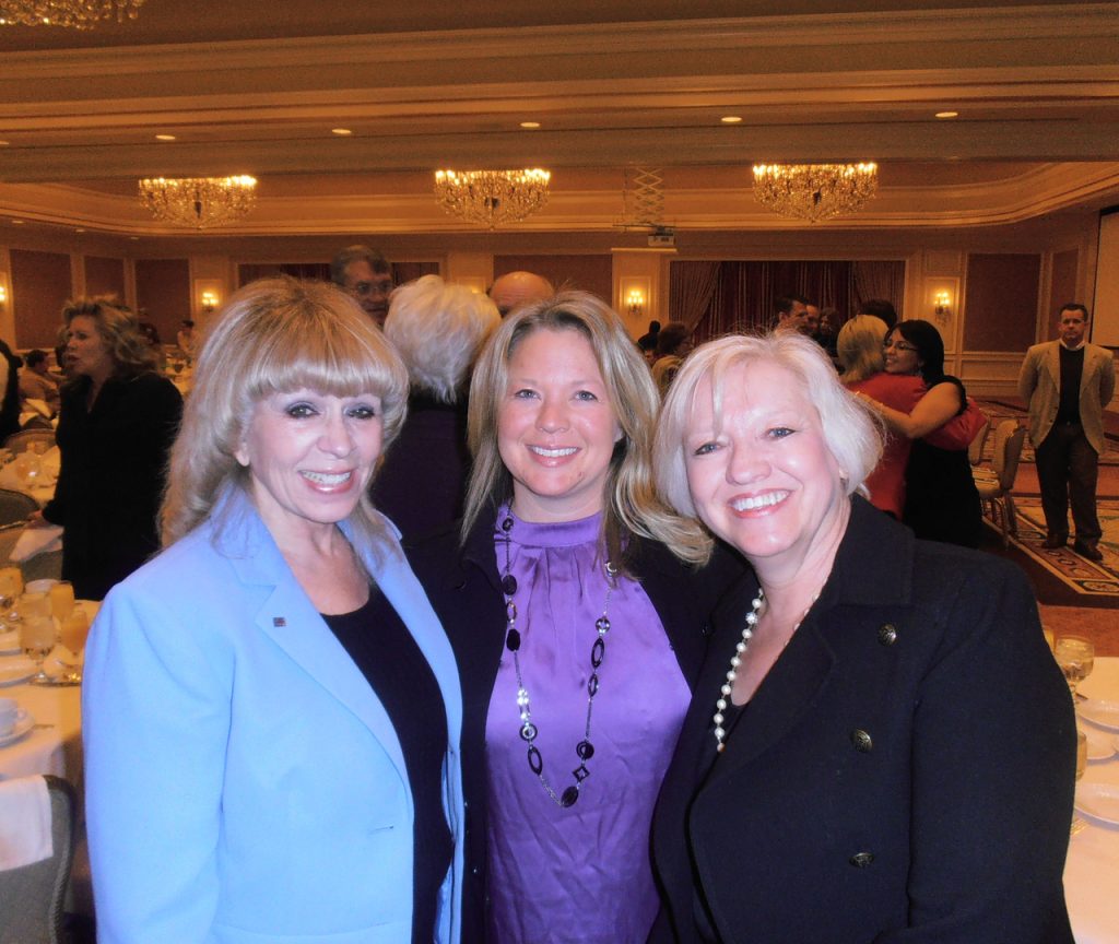 Three women in a room with a crowd of people.