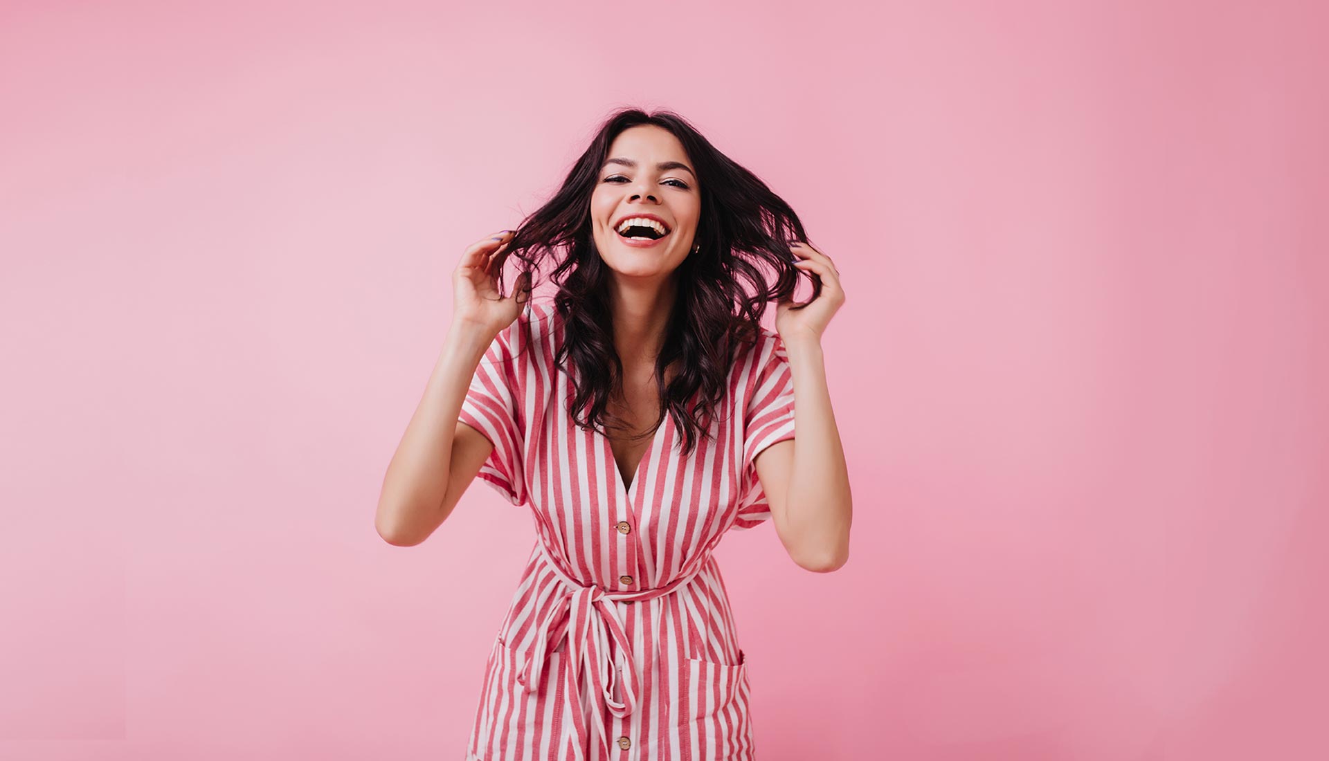 A woman in pink and white striped dress holding her hair.